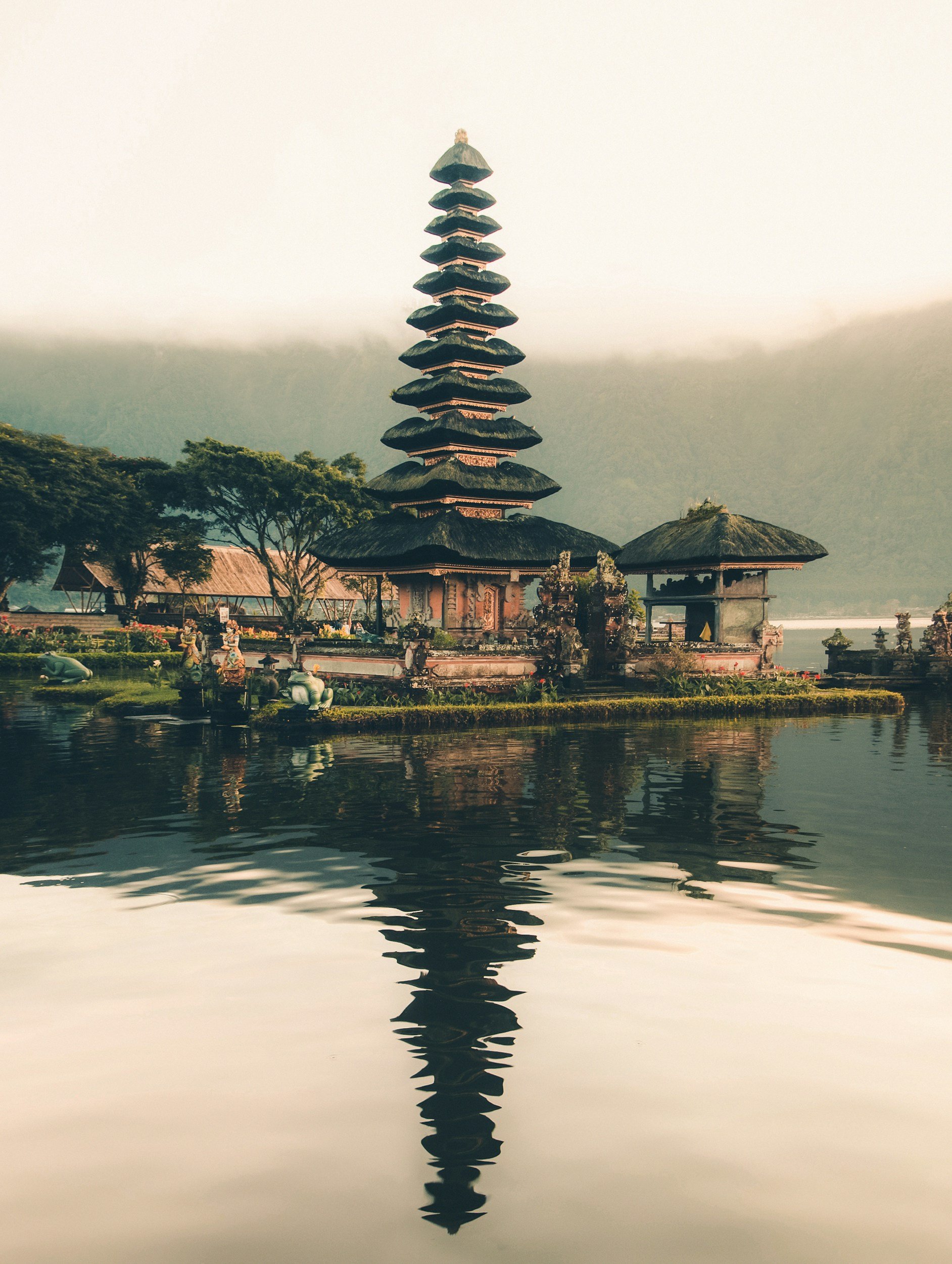 A traditional multi-tiered pagoda with nine levels, situated on a small island surrounded by water, with lush green trees and misty mountains in the background.